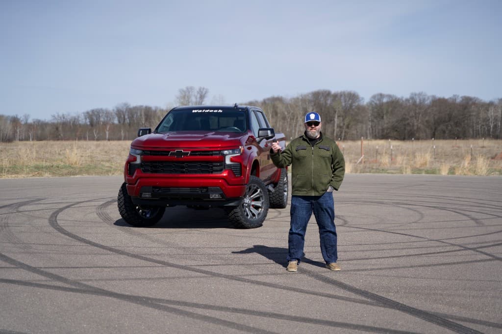 A man holding the keys beside a Radiant Red custom Chevy Silverado 1500 with a Waldoch Rampage conversion